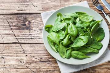 Fresh spinach leaves in bowl on rustic wooden table. Copy space