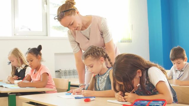 Teacher helping young schoolchildrens with writing lesson