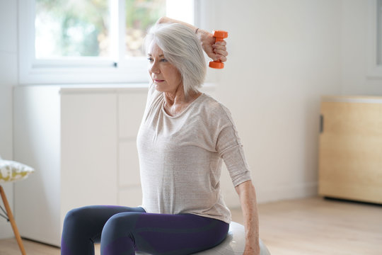  Attractive elderly woman exercising at home with swiss ball