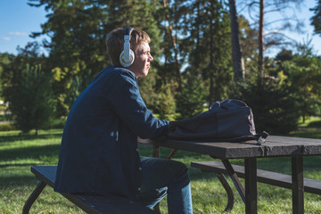 Fototapeta premium Concerned teenager listening to music with his headphones while sitting alone at a picnic table.