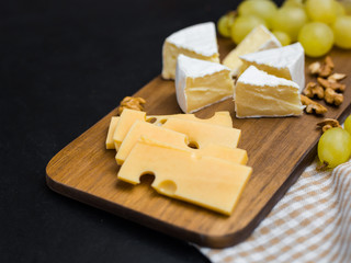 Slice of cheese, nuts and grapes on wooden cutting board. Camembert cheese and edam cheese. Food for wine and romantic