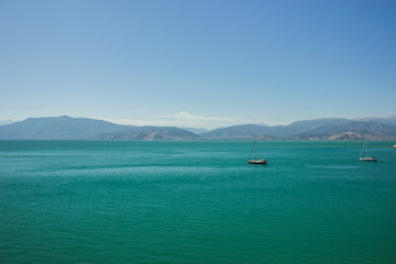Mediterranean landscape and seascape with ships and boats on vivid green and blue water surface and...