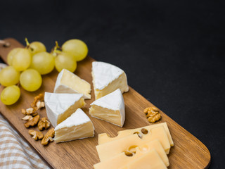Slice of cheese, nuts and grapes on wooden cutting board. Camembert cheese and edam cheese. Food for wine and romantic