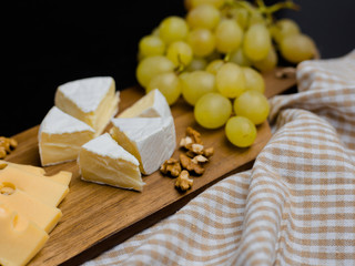 Slice of cheese, nuts and grapes on wooden cutting board. Camembert cheese and edam cheese with plaid fabric. Food for wine and romantic