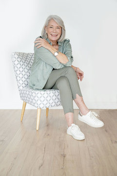 Beautiful Senior Woman Sitting On Armchair Infront Of White Background