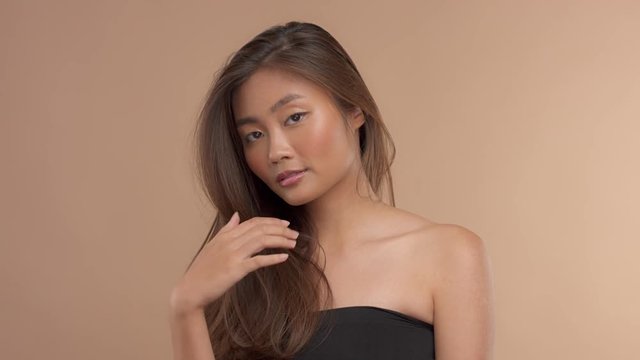 studio beauty hair video. Thai asian model with straight hair slow motion touchiing it and smiling