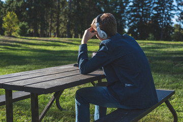 Concerned teenager listening to music with his headphones while sitting alone at a picnic table.