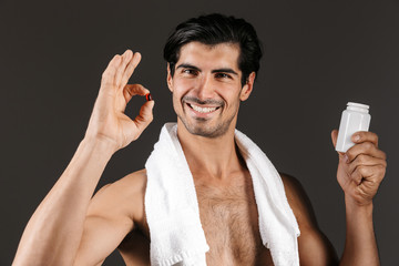 Handsome young man isolated over dark background with towel holding pills vitamins.