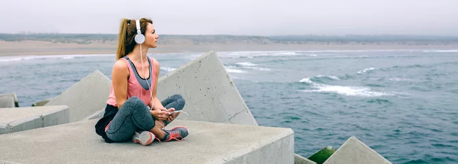 Gordijnen Sitting sportswoman with headphones watching the sea © David Pereiras