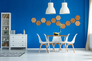 White furniture, wooden table and cork on blue wall in fancy dining room interior
