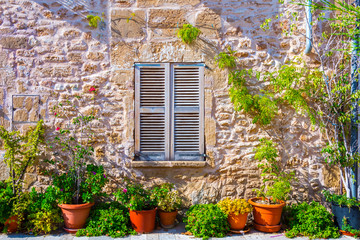 Fototapeta na wymiar The facade of an old stone house with wooden brown shutter and flowerpots. Majorca. Spain.