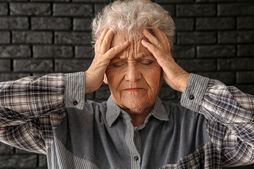 Senior woman suffering from headache on dark background