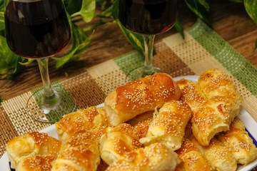Homemade pastry with sesame and cheese and glass of wine of blackberry. Table with vintage bamboo mat and liana vine in the background.