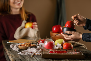 Woman dipping apple into bowl with caramel on wooden table