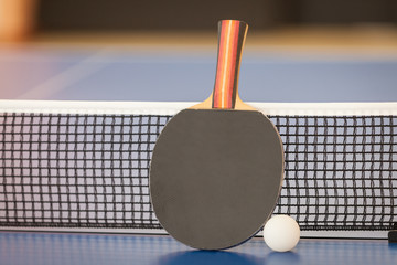 Table tennis or ping pong racket and ball on blue table, net