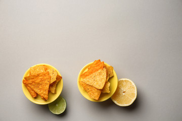 Tasty corn chips with citrus fruits on grey background