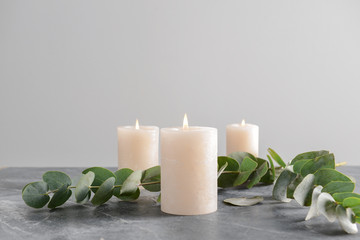 Fototapeta na wymiar Burning candles with eucalyptus branches on grey table