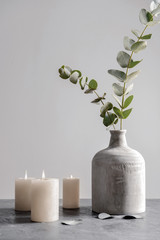 Burning candles and vase with eucalyptus branches on grey table