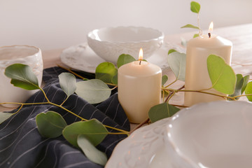 Burning candles with eucalyptus branches and dishware on wooden table