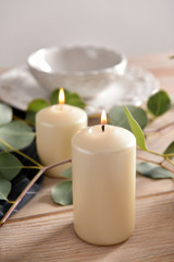 Fototapeta na wymiar Burning candles with eucalyptus branches on wooden table