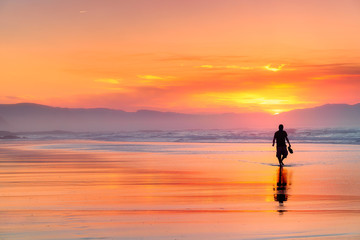 Fototapeta na wymiar lonely person walking on beach at beautiful red sunset