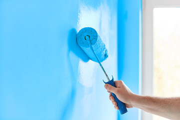 Male hand painting wall with paint roller. Painting apartment, renovating with blue color paint