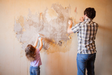 Father and daughter repairing wall, holding putty knife