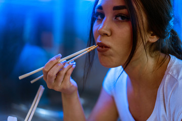 Close up of young attractive woman eating asian food with chopsticks at cafe.