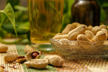Beer in bottle and glasses and peanuts in crystal bowl. Table with vintage bamboo mat and liana vine in the background.