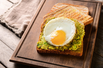 Tasty toasted bread with avocado and fried egg on wooden board