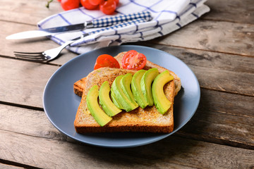 Plate with tasty toasted bread and avocado on wooden table