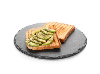 Slate plate with tasty toasted bread and avocado on white background