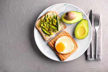 Plate with toasted bread, avocado and fried egg on grey table
