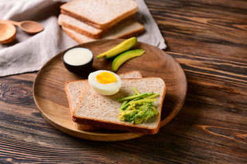 Delicious toasted bread with avocado and boiled egg on wooden board