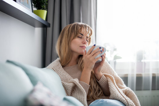 Happy woman in soft sweater relaxing at home with cup of hot tea or coffee