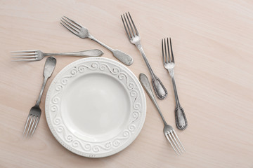 Plate and forks on light wooden background, flat lay
