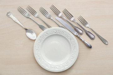 Plate and forks on light wooden background, flat lay
