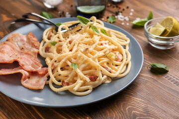 Plate with delicious spaghetti and bacon on wooden table, closeup