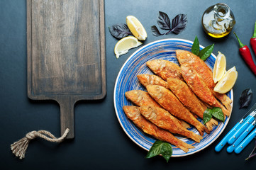 Fried seafood (‘red mullet’, ‘barbule’) on on a blue plate, dark background. Next cutting board