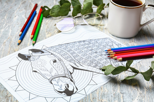 Adult anti stress coloring picture, pencils and cup of coffee on table
