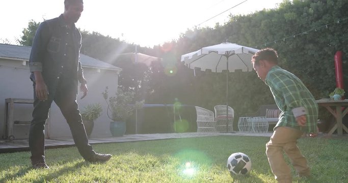 African American father and son playing football in yard