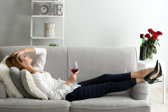 Tired Woman With Glass Of Wine On Sofa At Home