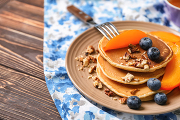 Hot tasty pancakes with sliced persimmon, blueberries and walnuts on plate