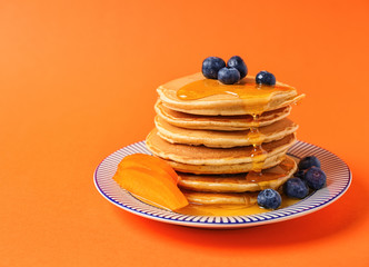 Plate with hot tasty pancakes, sliced persimmon and blueberries on color background