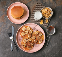 Hot tasty pancakes with banana slices and glass of milk on grey table