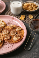 Hot tasty pancakes with banana slices and glass of milk on grey table