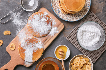 Hot tasty pancakes with banana slices, honey and sugar powder on grey table