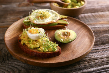 Wooden plate with delicious avocado toasts on table, closeup