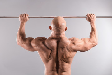 Muscular bodybuilder training on grey background