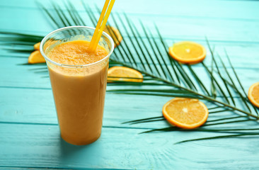 Plastic cup of tasty orange smoothie on color wooden table